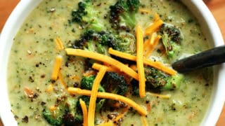 A bowl of Creamy Vegan Broccoli Soup topped with roasted broccoli and vegan cheese shreds.