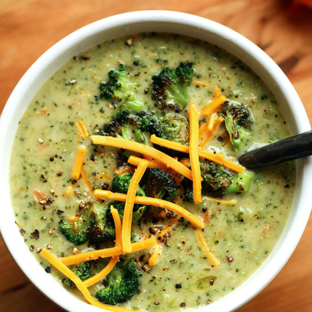 A bowl of Creamy Vegan Broccoli Soup topped with roasted broccoli and vegan cheese shreds.