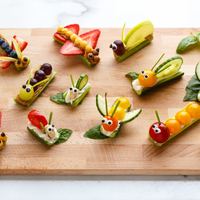 Fruit and vegetable bug snacks arranged on a wood board.