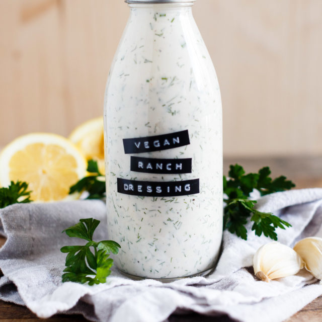 Bottle of homemade vegan ranch dressing shown on a grey kitchen towel and wood background.