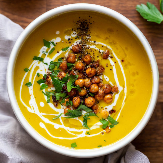 Top view of a bowl of chickpea turmeric soup topped with a swirl of coconut cream, crispy spiced chickpeas, and chopped herbs.