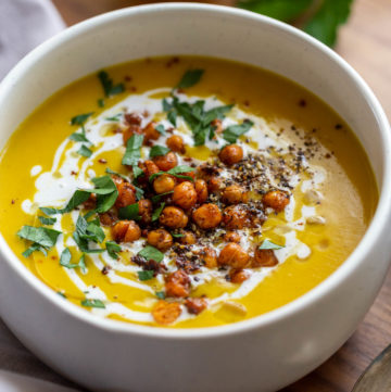 Bowl of chickpea turmeric soup topped with a swirl of coconut cream, crispy spiced chickpeas, and chopped herbs.